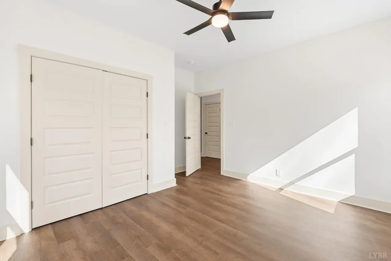 A bright, empty room with light wood floors, white walls, double closet doors, and an open doorway leading to a hallway.