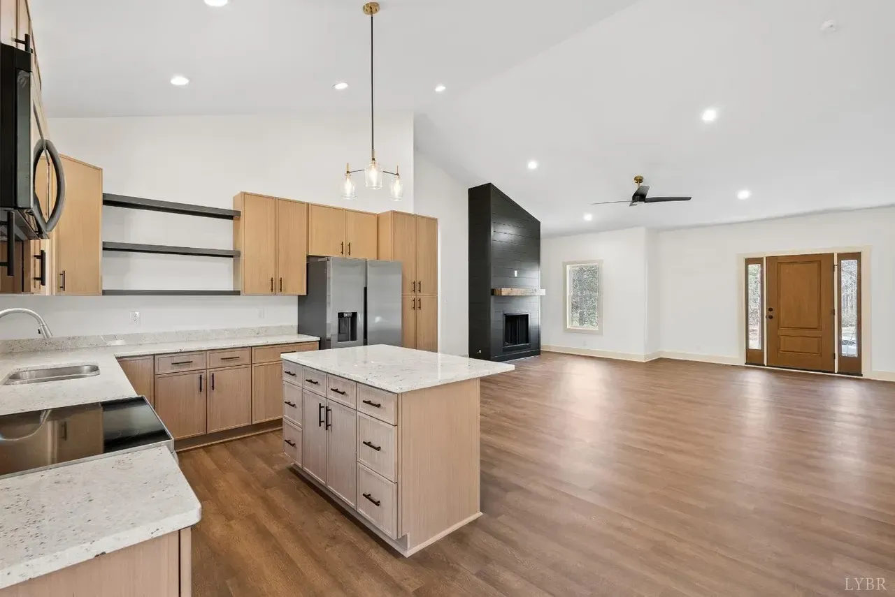 A modern, open-concept kitchen and living area with light wood cabinets, white countertops, and a black fireplace.