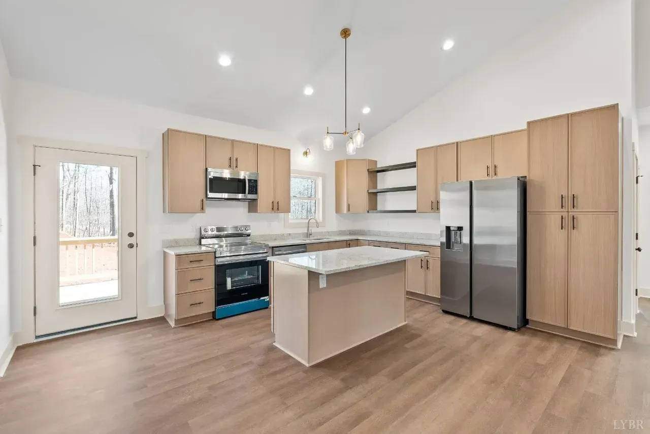 A modern kitchen with light wood cabinets, stainless steel appliances, a central island, and wood-look flooring.