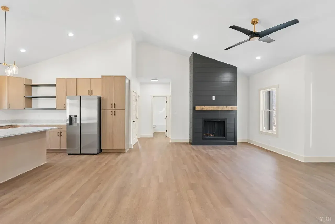A modern open-plan living and kitchen area with light wood flooring, light cabinetry, and a dark grey fireplace feature.