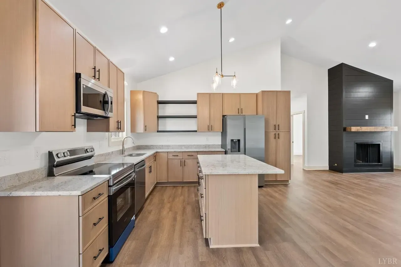 Modern kitchen with light wood cabinets, white countertops, stainless appliances, a central island, and a black fireplace.