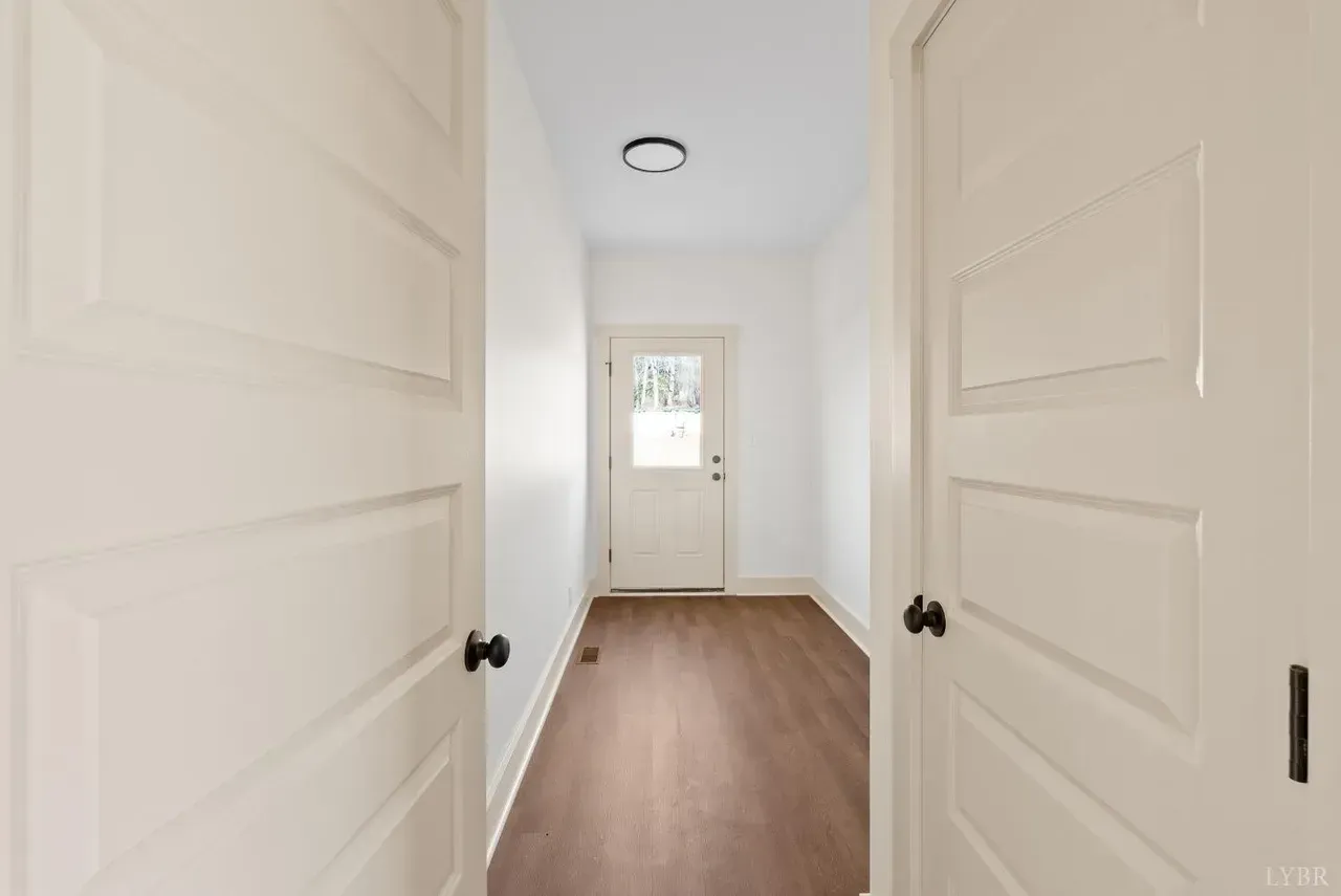 Interior view through open double doors into a hallway leading to a white exterior door with glass pane.