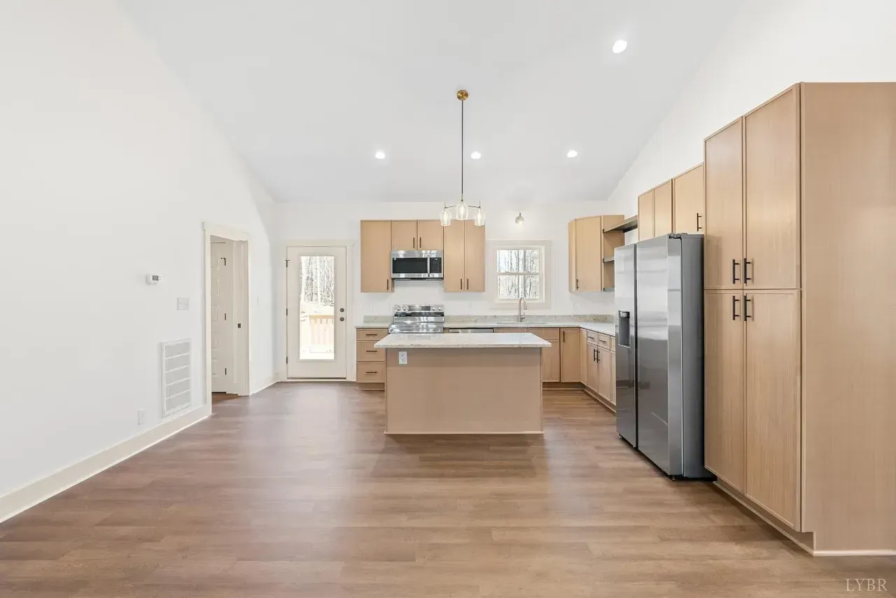 Modern kitchen with light wood cabinets, stainless steel refrigerator, white countertops, island, and vaulted ceiling.