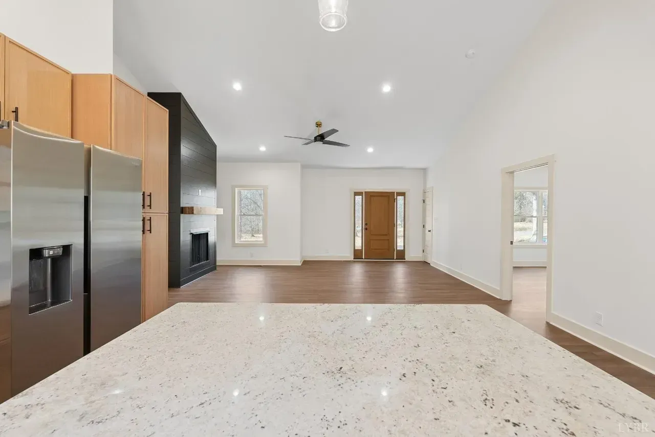 A modern kitchen island with a speckled countertop faces a living area with a fireplace, high ceilings, and wood floors.