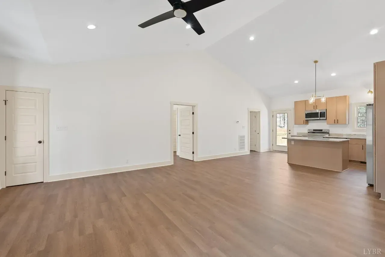 A bright, open-concept living area with vaulted ceilings, wood-look flooring, and a kitchen with light wood cabinetry.
