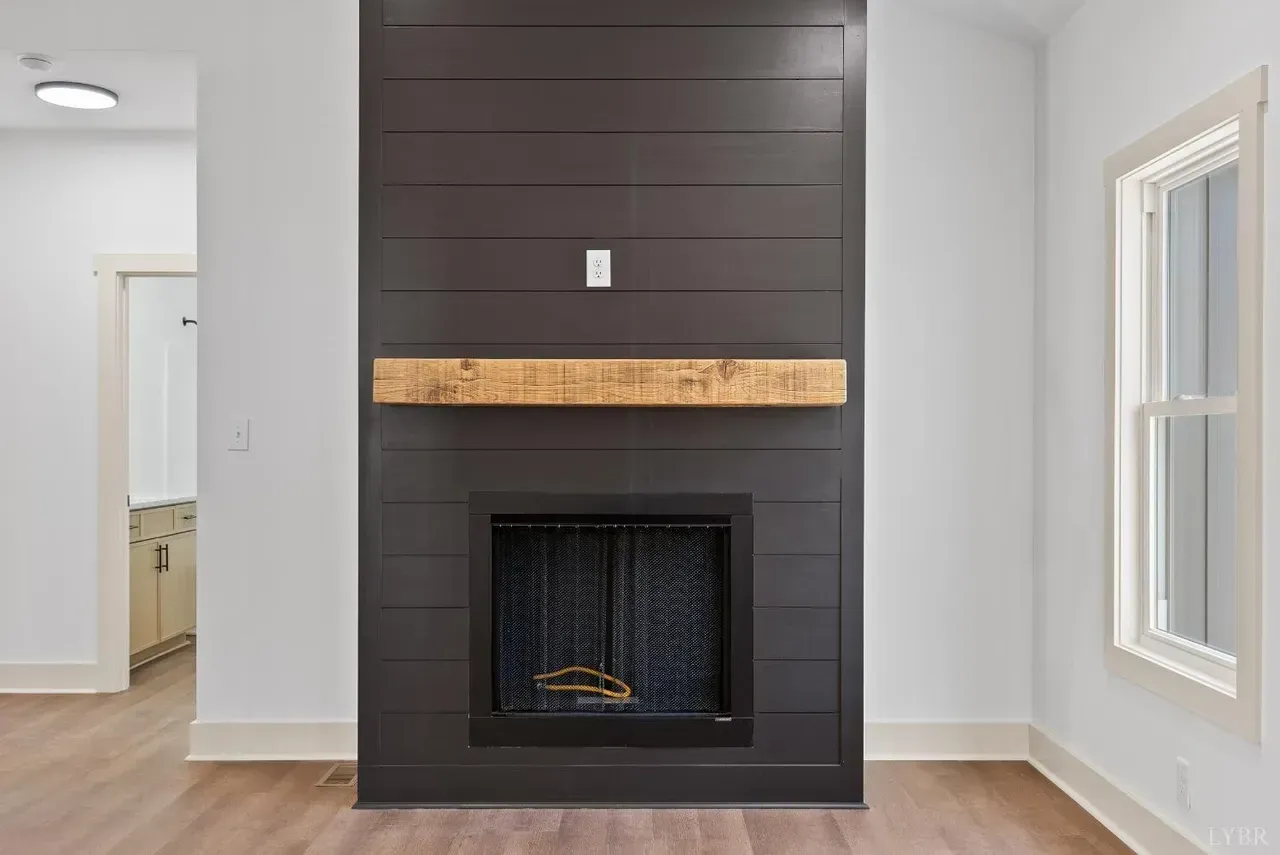 A dark gray, wood-paneled fireplace surround with a natural wood mantel, centered on a white wall in a room.