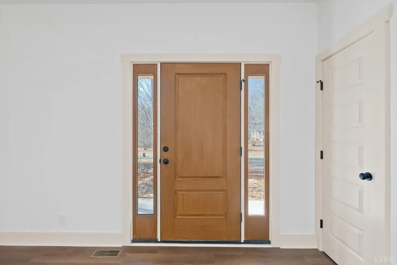 A brown wooden front door with side windows and a matching interior door on the right against a white wall.