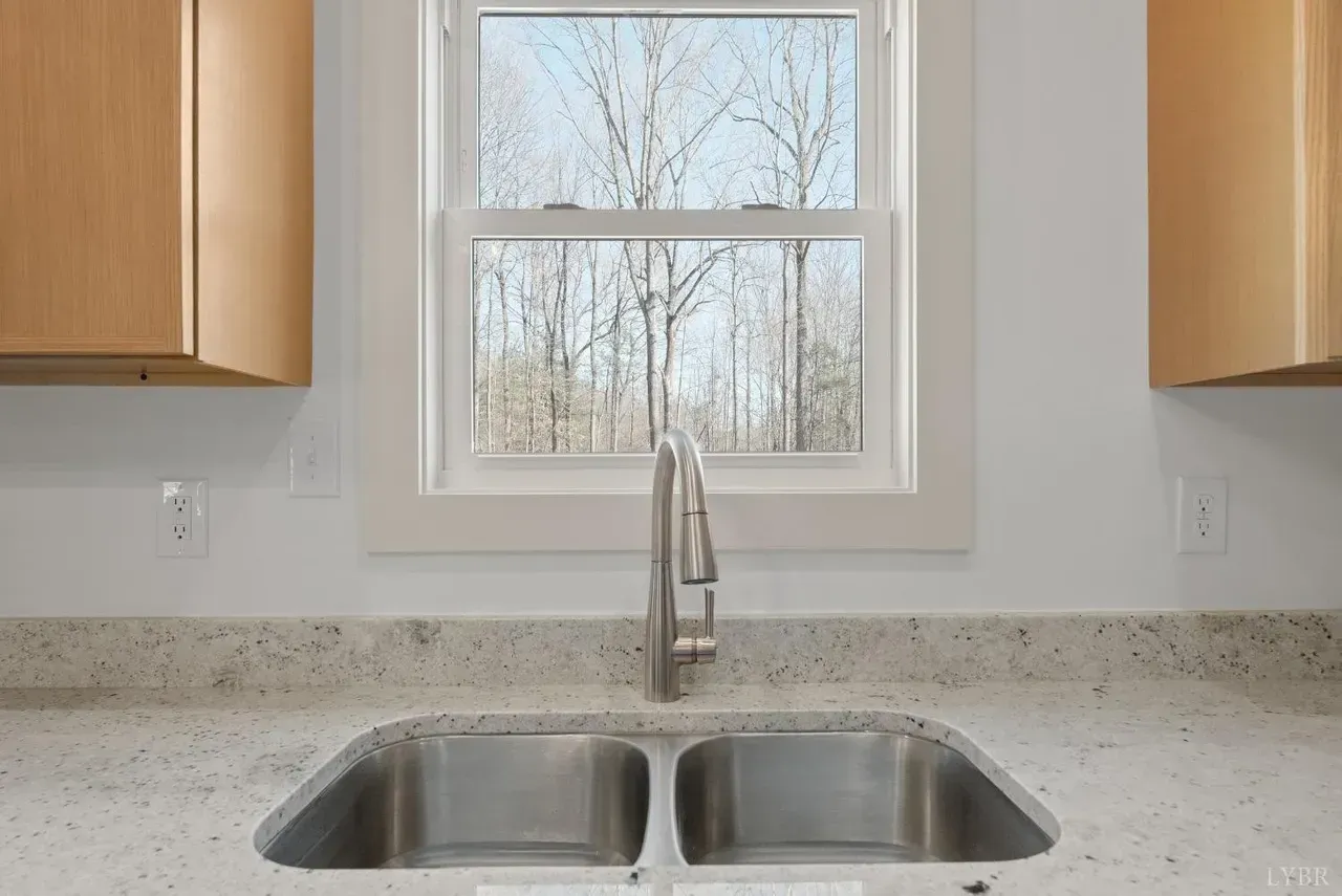 A kitchen sink with a stainless steel faucet in front of a window looking out onto a forest.