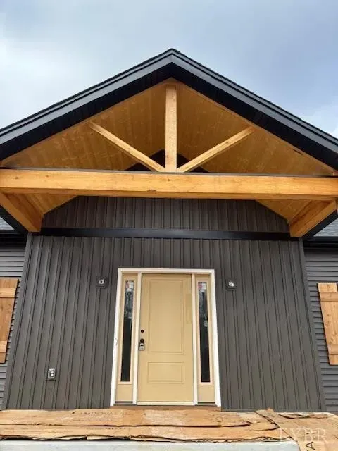 Modern home entrance with a wood-accented gable, vertical dark gray siding, and a tan front door with side windows.