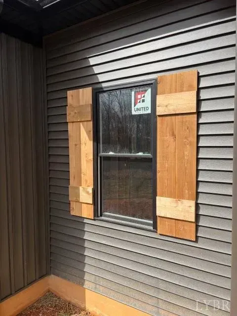 A vertical window with natural wood shutters mounted on gray horizontal vinyl siding on the exterior of a house.