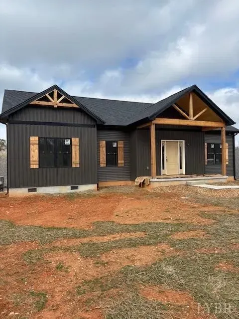 A new house with dark vertical siding, a front porch with wooden beams, light wood accents, and a large front yard.