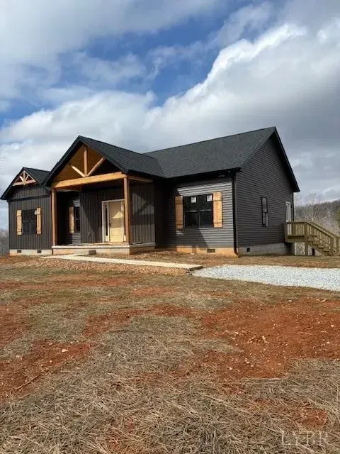 A newly constructed one-story home with dark gray siding, a black roof, and wooden accents, set on a rural dirt lot.