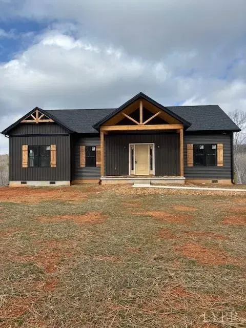 A modern, dark-sided single-story home with a light wood-trimmed entryway and gables under a cloudy sky.