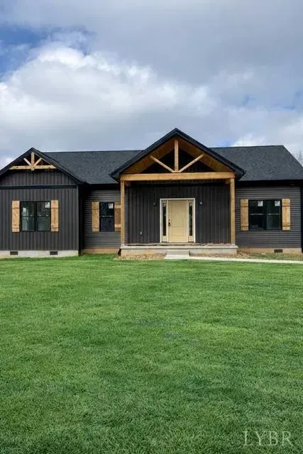 A dark-sided ranch house with wood-accented gables, a covered front porch, and a bright green lawn under a cloudy sky.