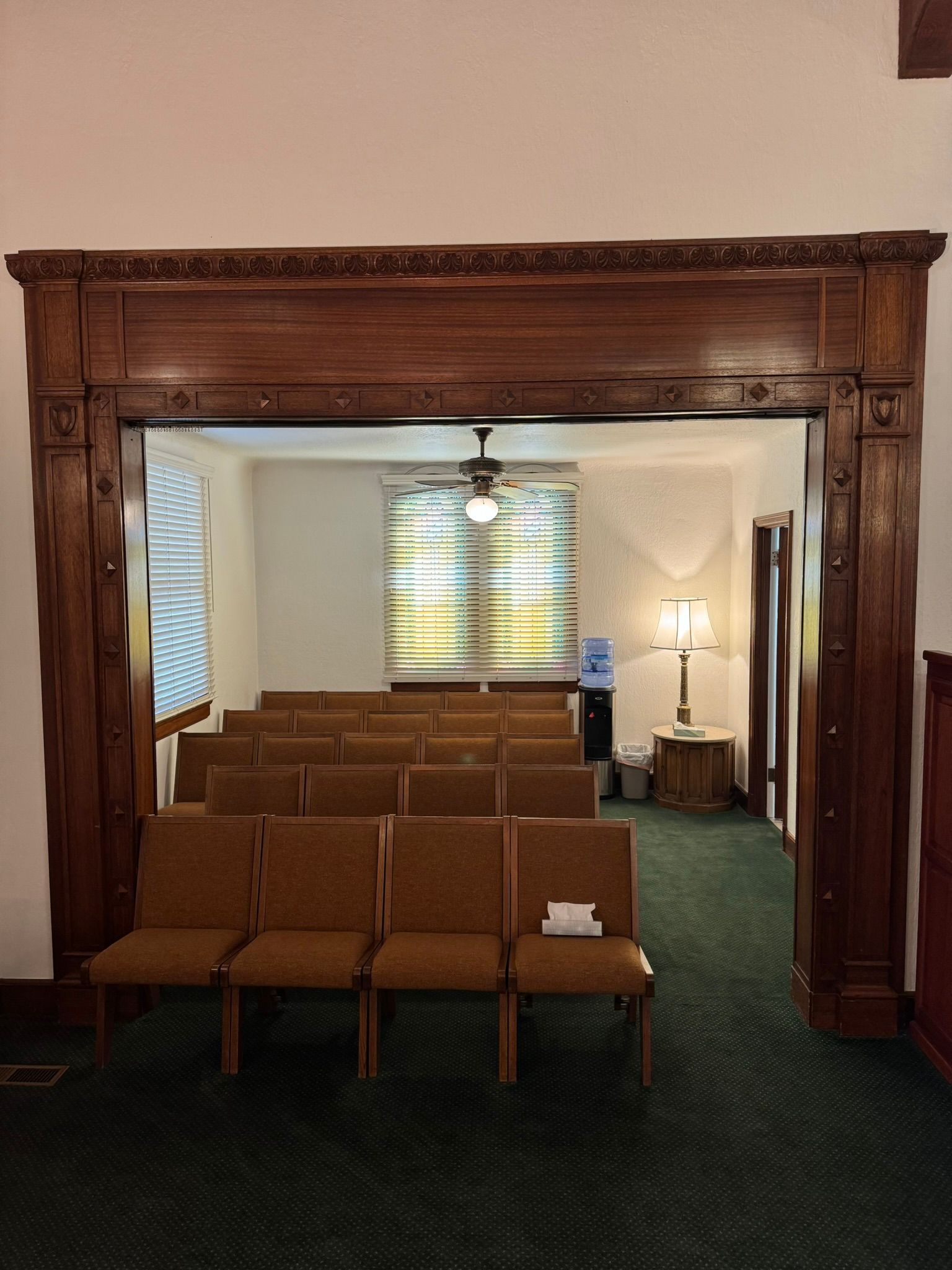 View into a room with rows of chairs, a decorative wooden frame, and a water cooler.