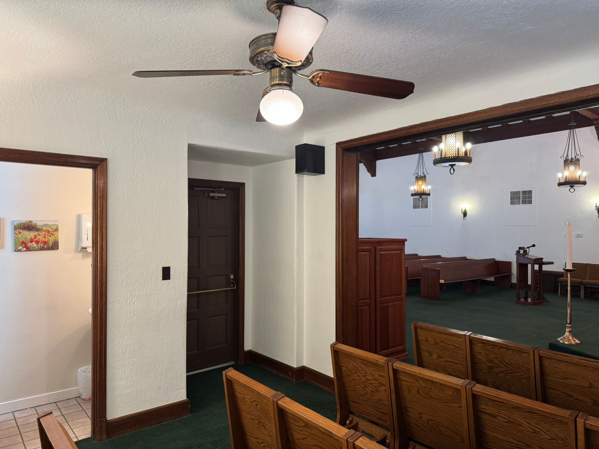 Interior of a chapel with rows of chairs facing a stage. A ceiling fan hangs above.