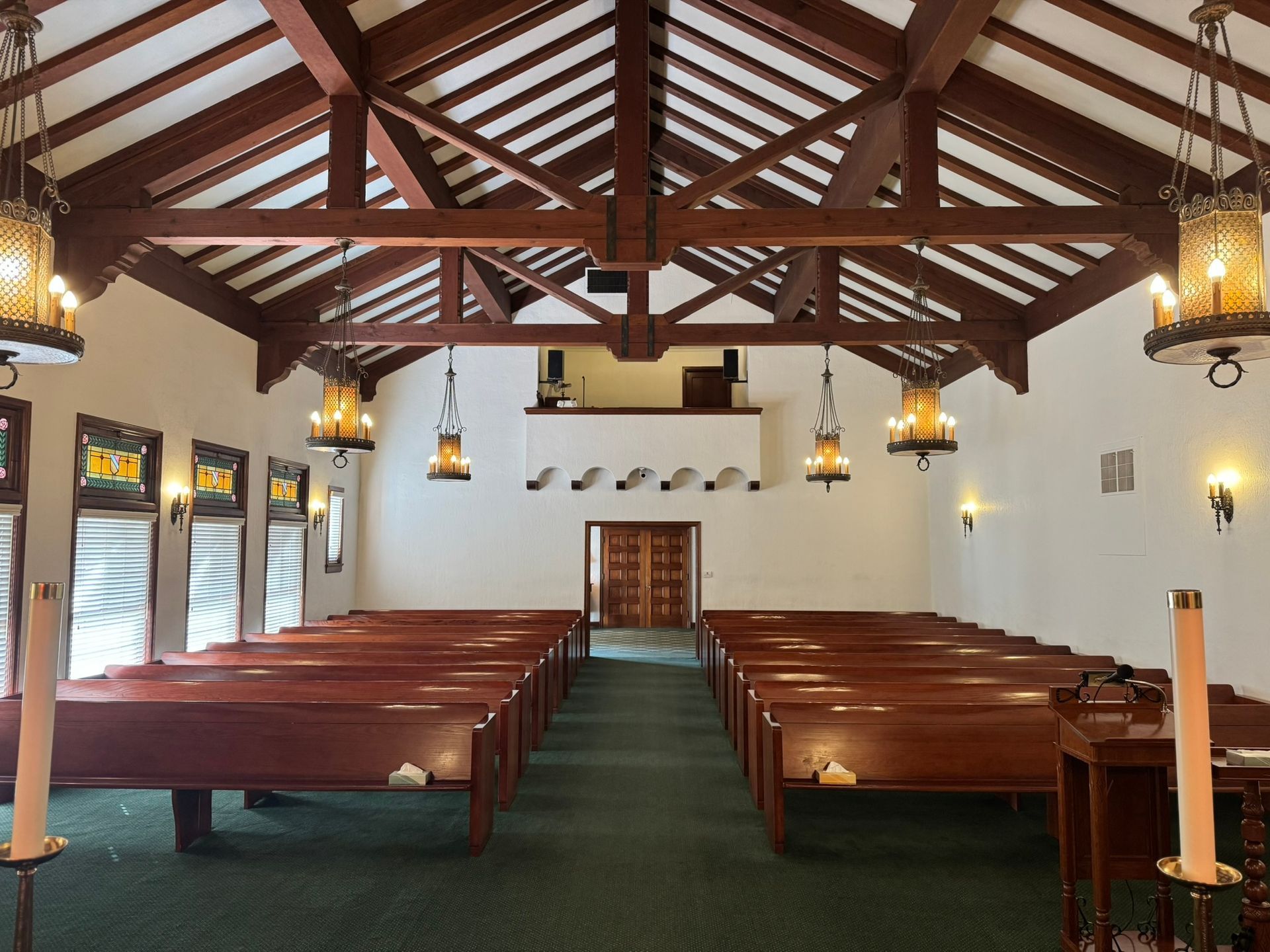 Interior view of a chapel with wooden pews, high wooden beams, and ornate hanging lights.