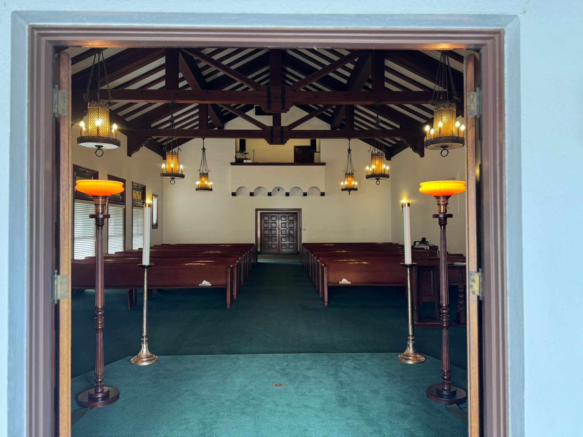 Interior of a chapel with pews, candles, and hanging lights, viewed from the doorway.