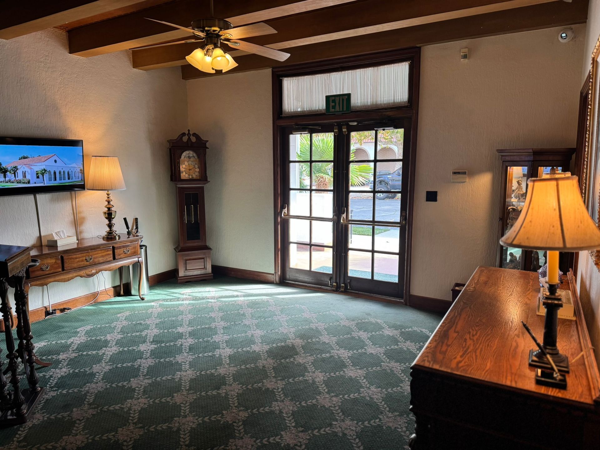 An antique-filled room with green patterned carpet, wood beams, and double doors to outside.