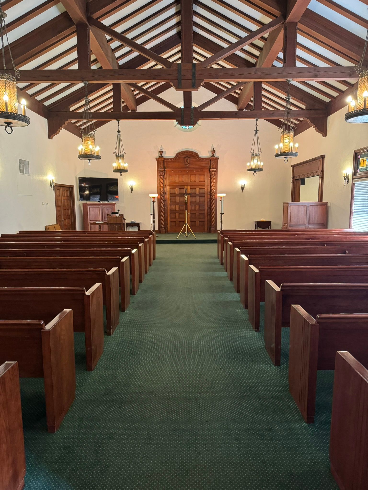 Interior view of a chapel with rows of wooden pews, green carpet, and a wooden ark in the background.