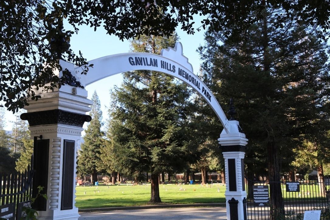 White arched entrance to a park with trees and green grass. Text reads: 