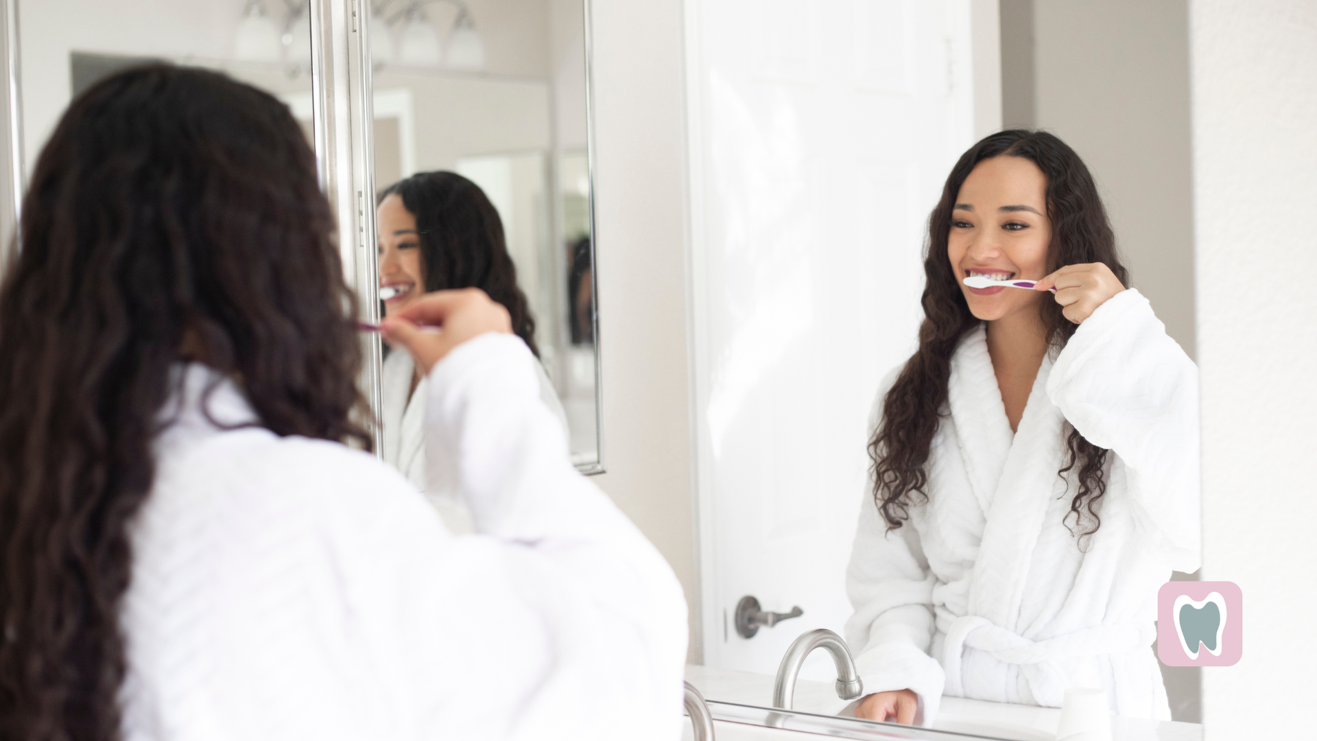 Woman in white robe brushing teeth in front of a mirror.