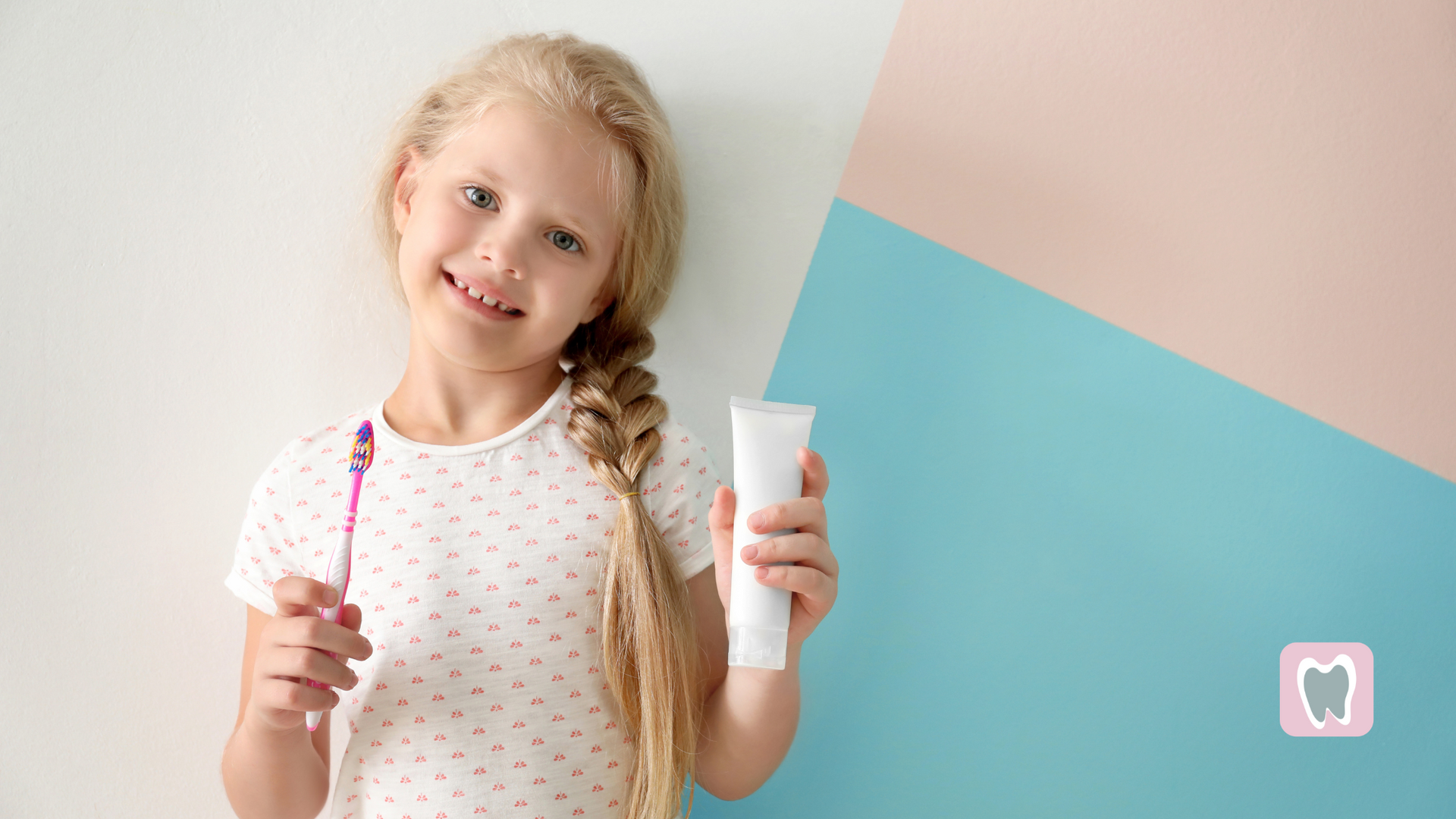 A little girl is brushing her teeth and holding a tube of toothpaste.