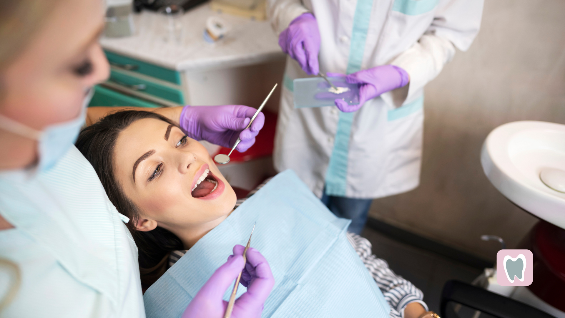 A woman is sitting in a dental chair while a dentist examines her teeth.