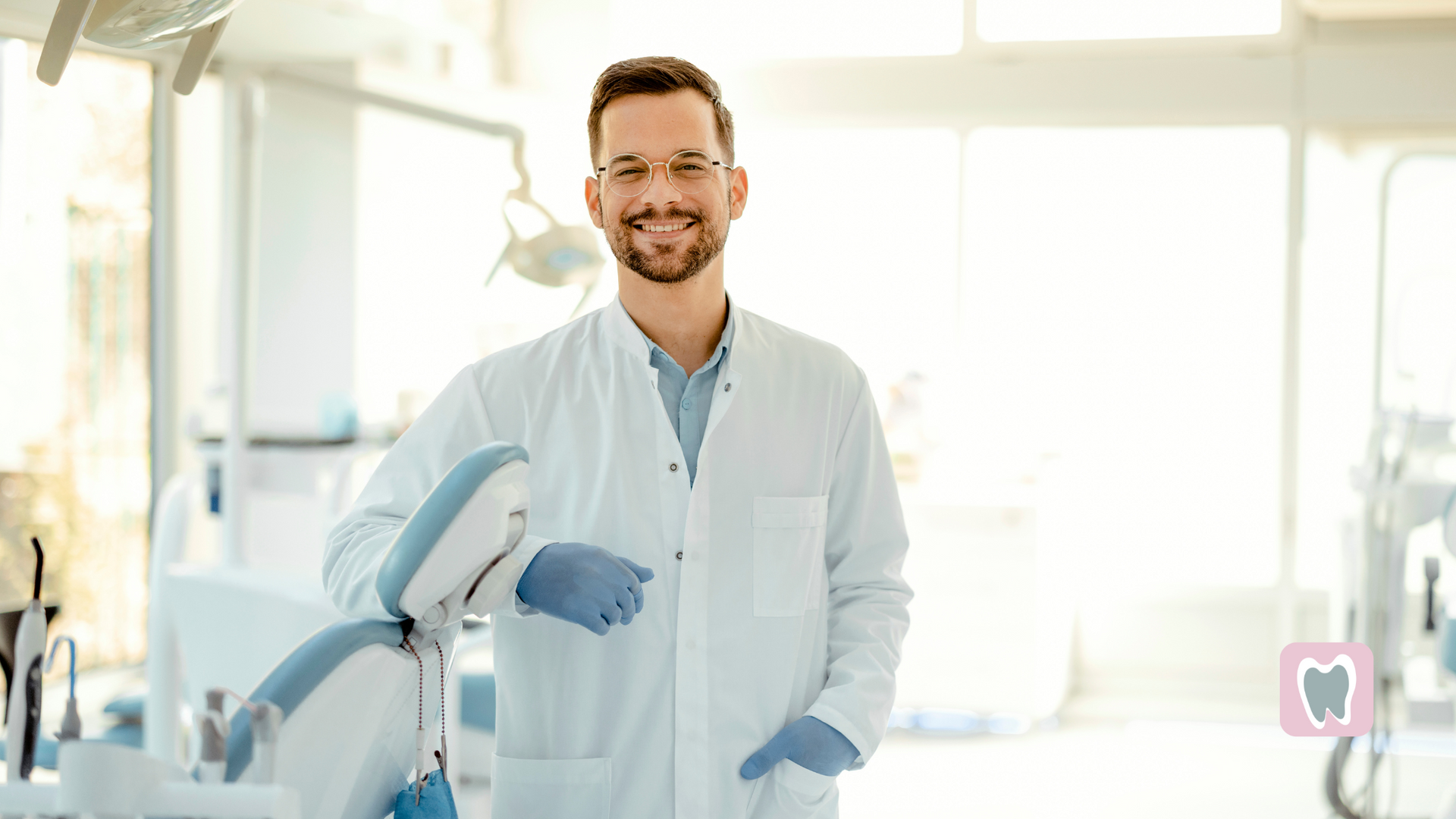 A dentist is smiling while holding a machine in a dental office.