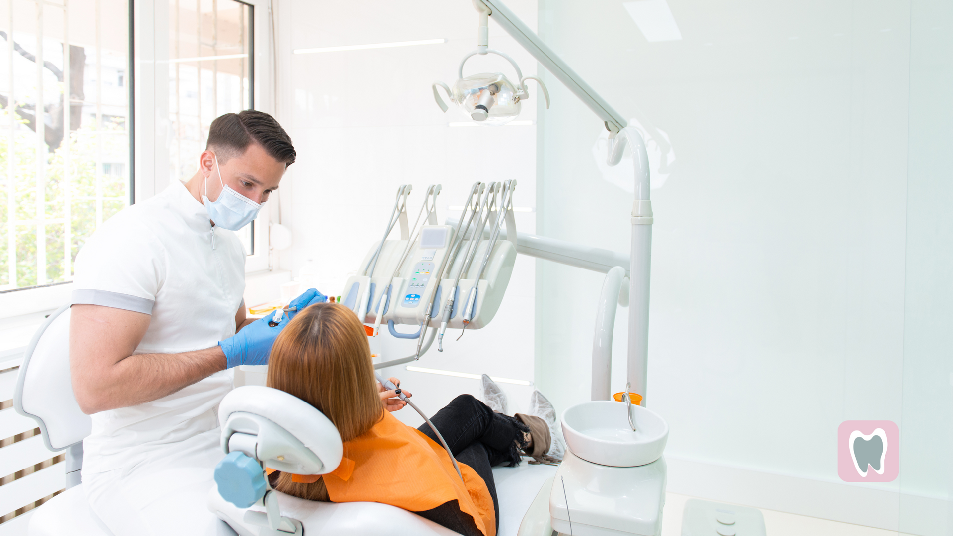 A woman is sitting in a dental chair while a dentist examines her teeth.