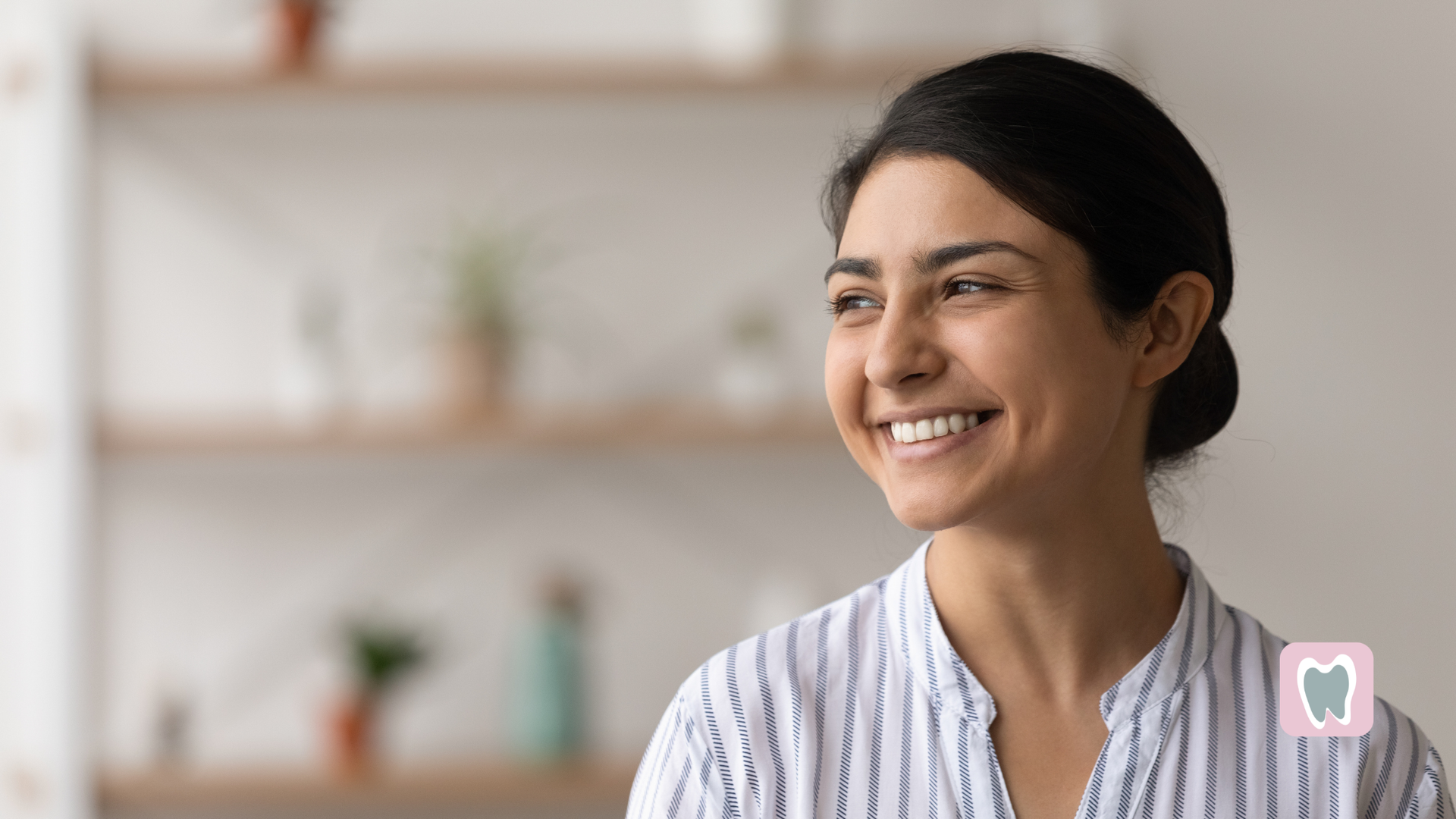 Woman smiling, looking to the side, wearing a striped shirt.  Blurred background with shelves.