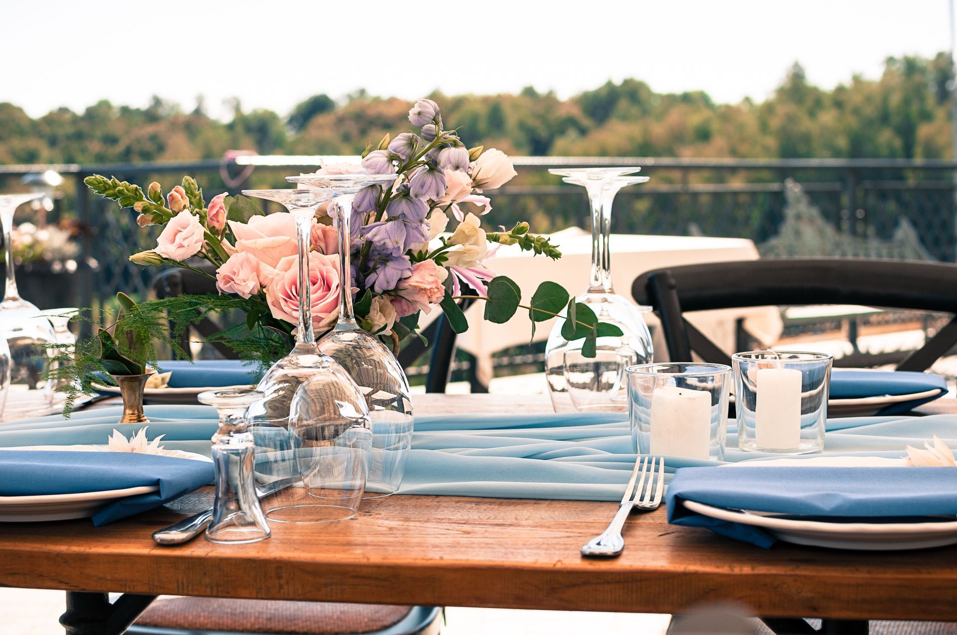 A wooden table with plates , napkins , glasses , and a vase of flowers on it.