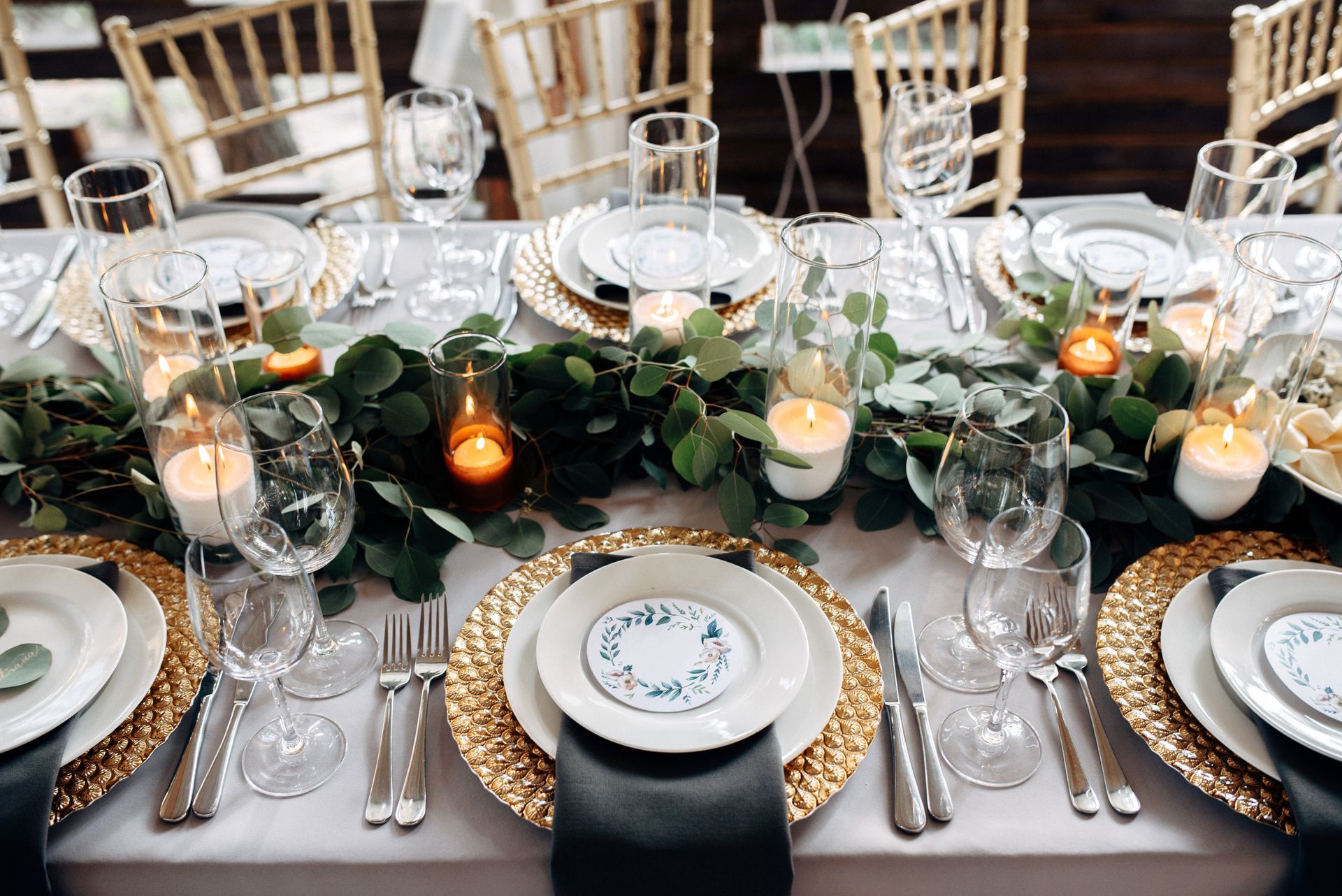 A long table set for a wedding reception with plates , glasses , silverware and candles.