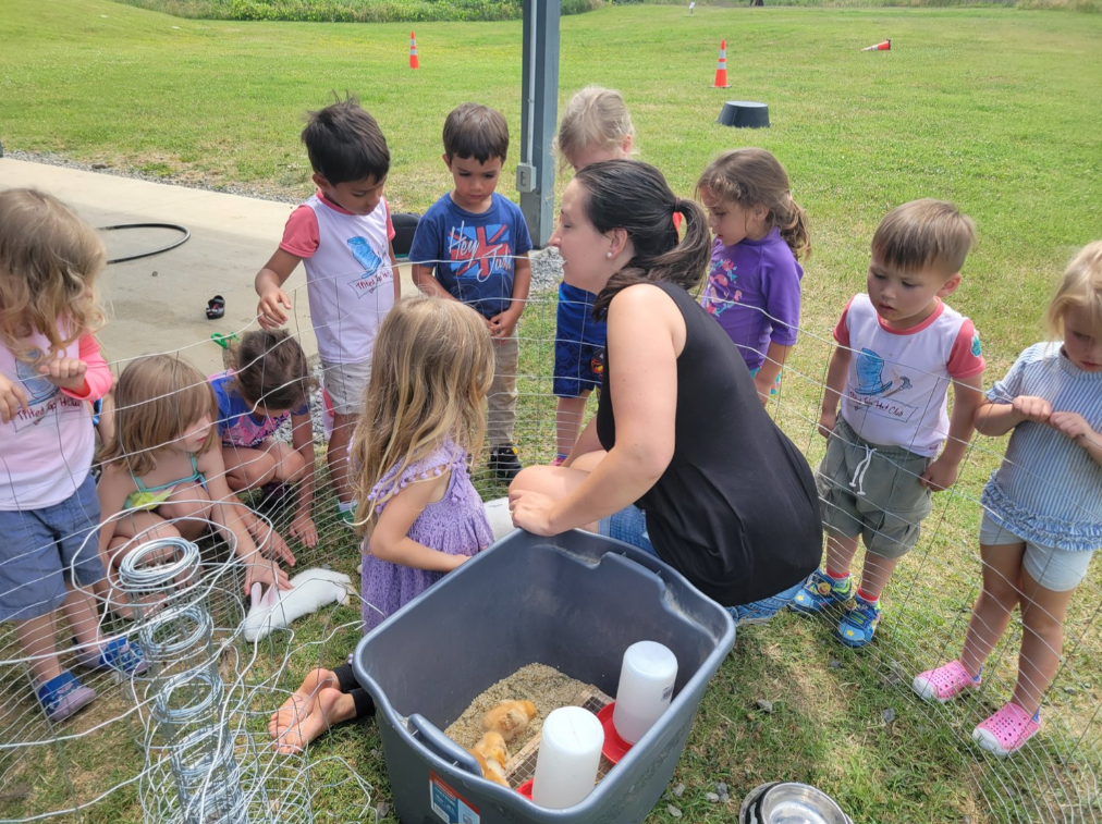 A woman is sitting in front of a group of children in a field.
