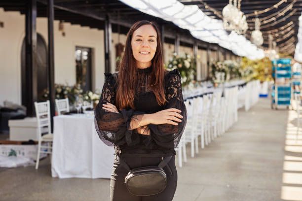 A woman is standing in front of a long row of white tables and chairs.