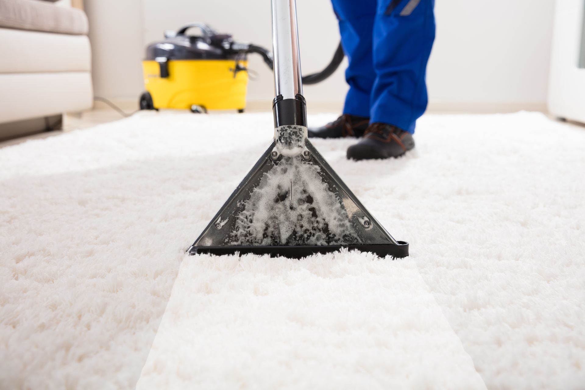 A man is cleaning a white carpet with a vacuum cleaner.