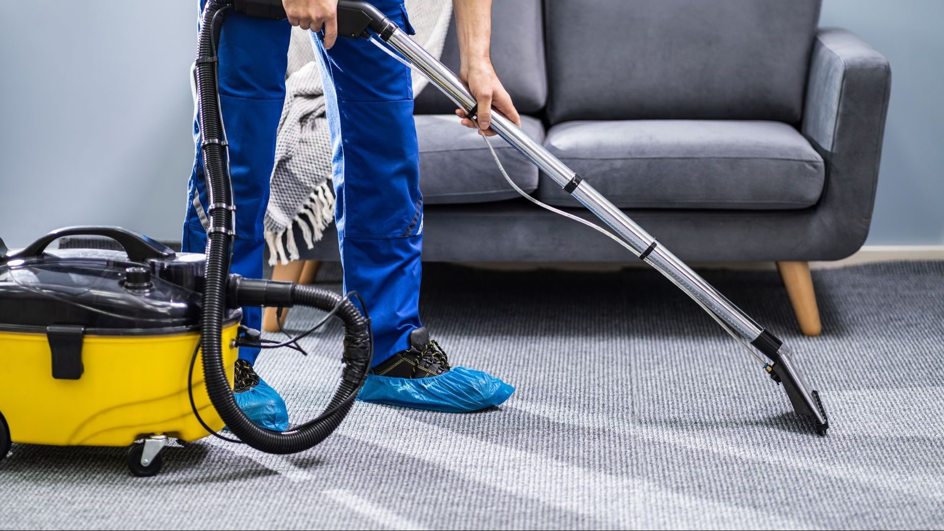 A man is using a vacuum cleaner to clean a carpet in a living room.