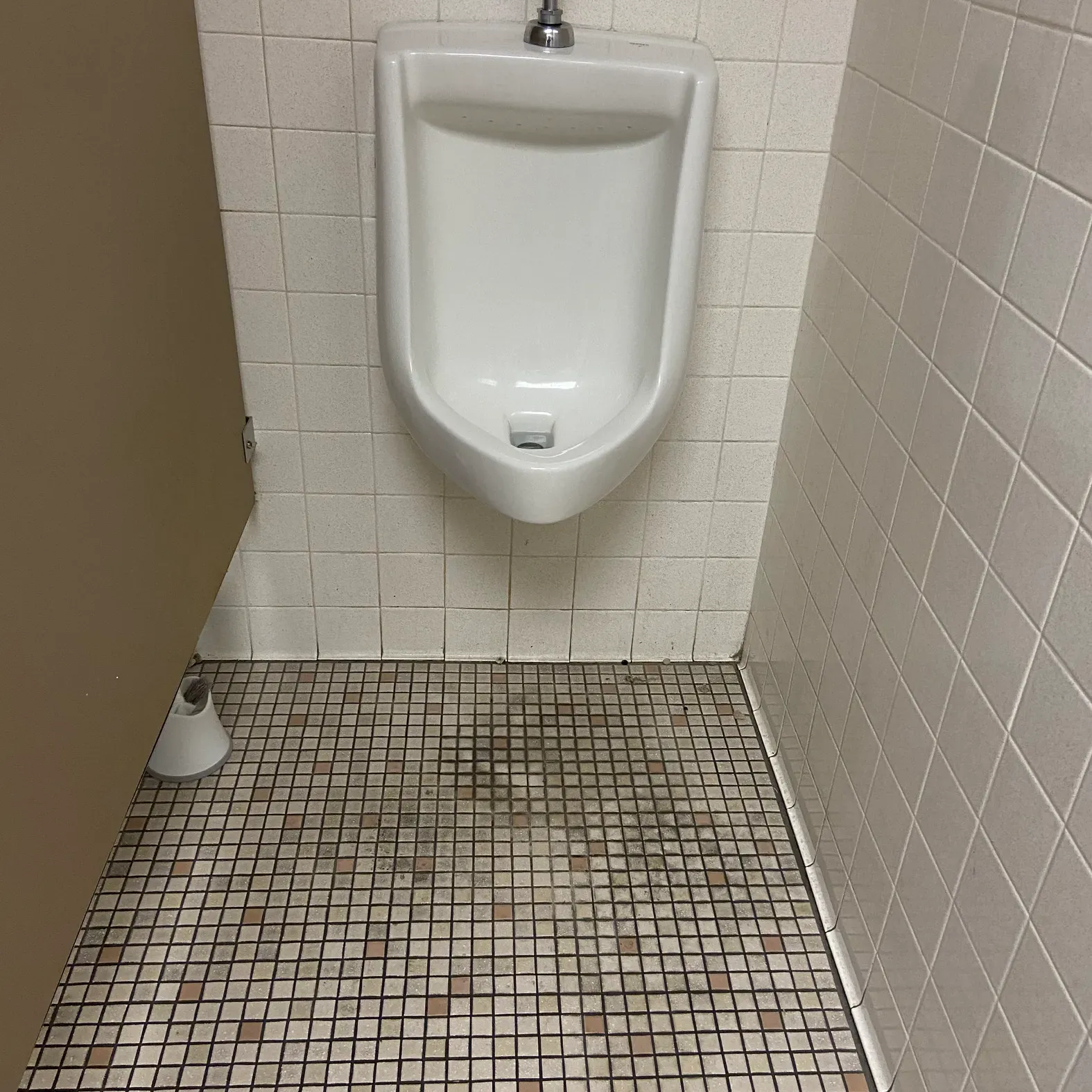 A urinal in a bathroom with a tiled floor