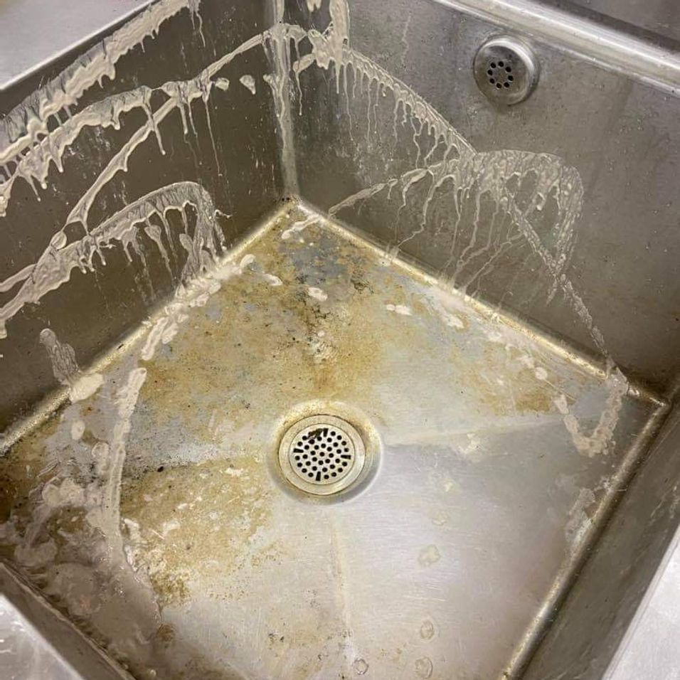 A very dirty stainless steel sink with a drain.