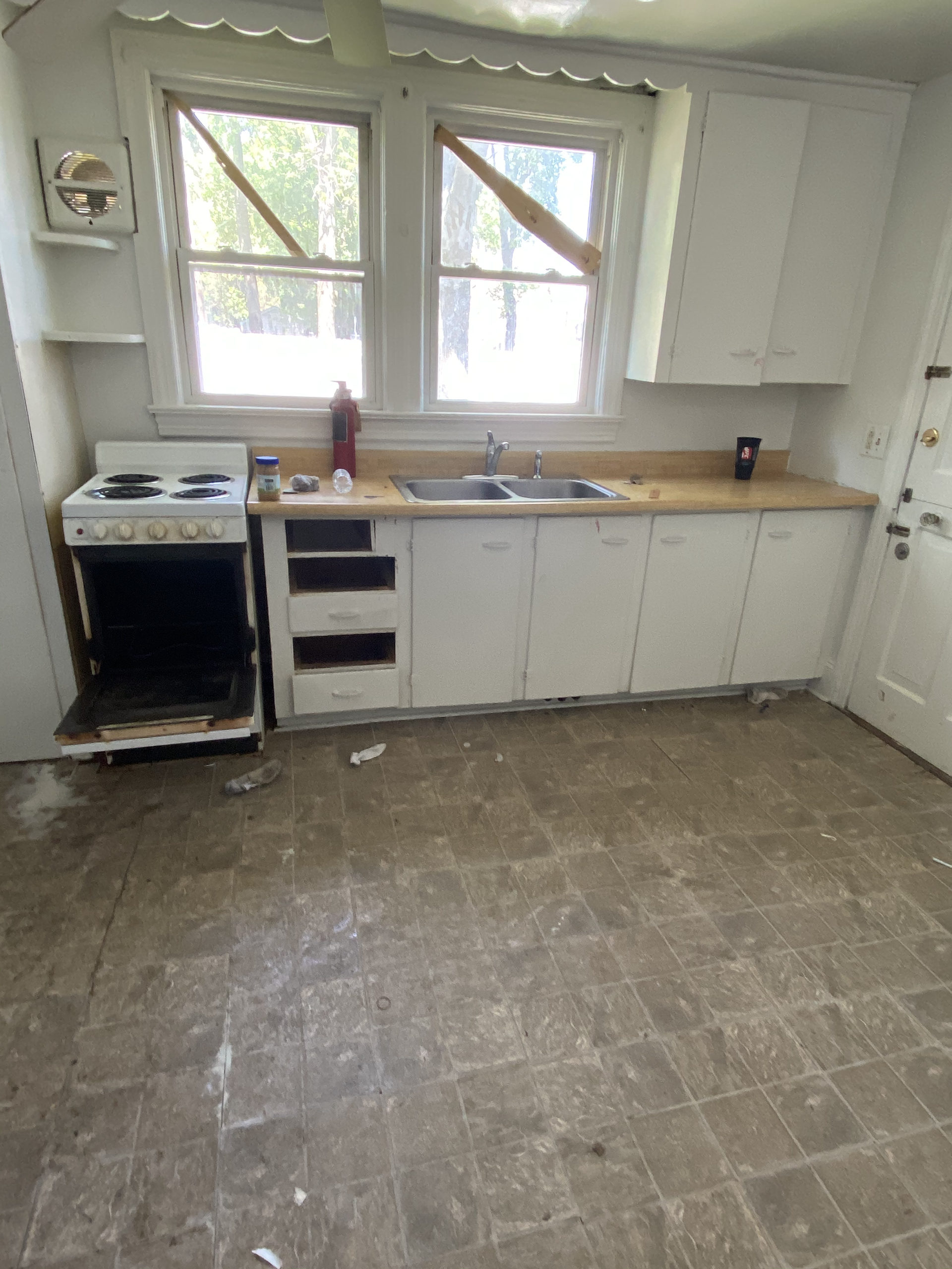 An empty kitchen with a stove , sink , and window.