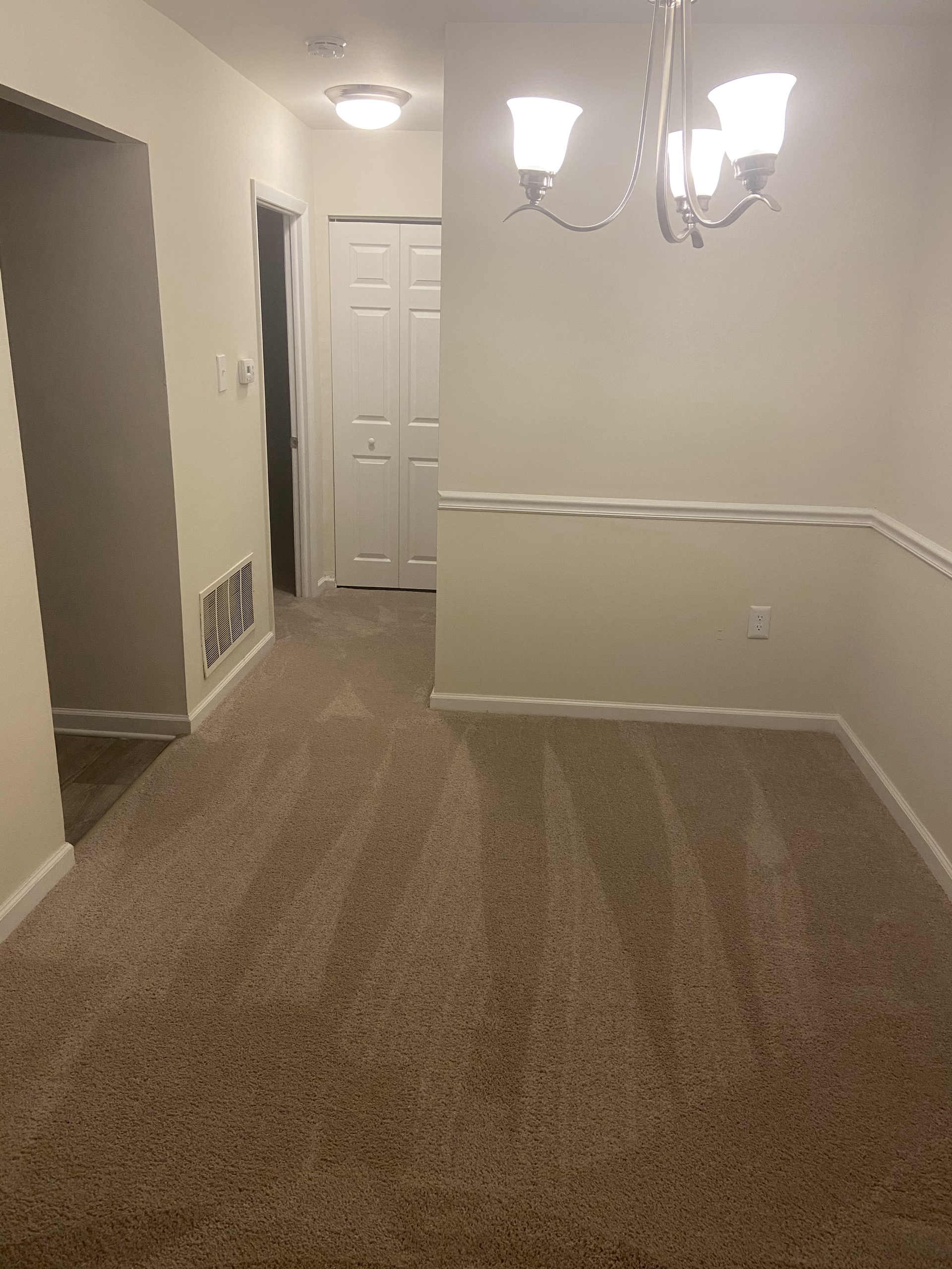 An empty dining room with a chandelier and a carpeted floor.