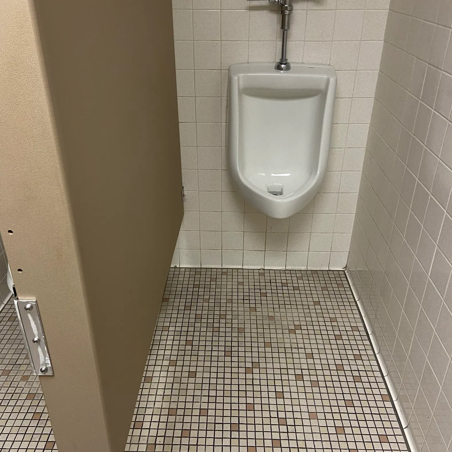 A urinal in a bathroom with a tiled floor