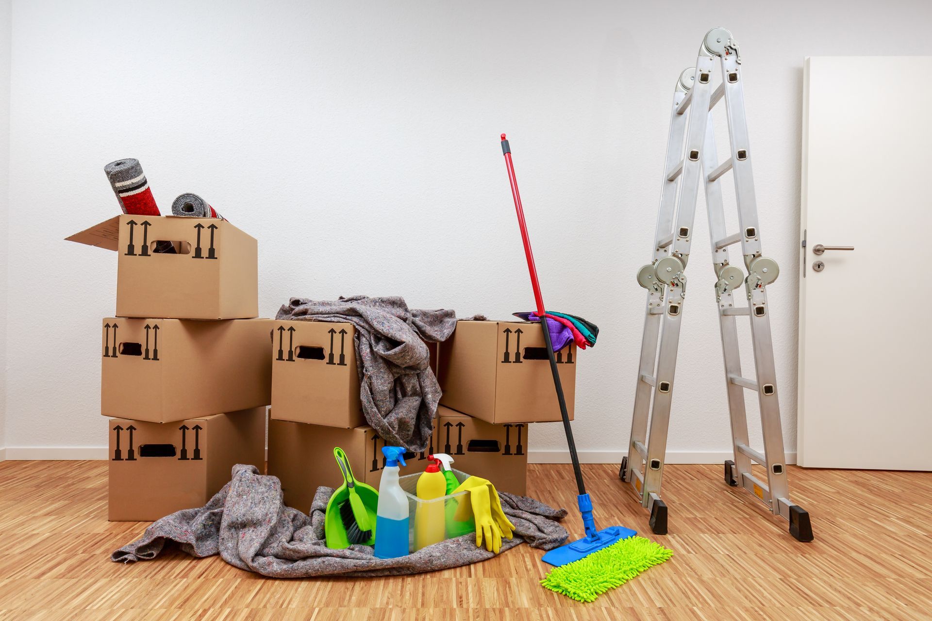 A room filled with cardboard boxes , cleaning supplies , and a ladder.