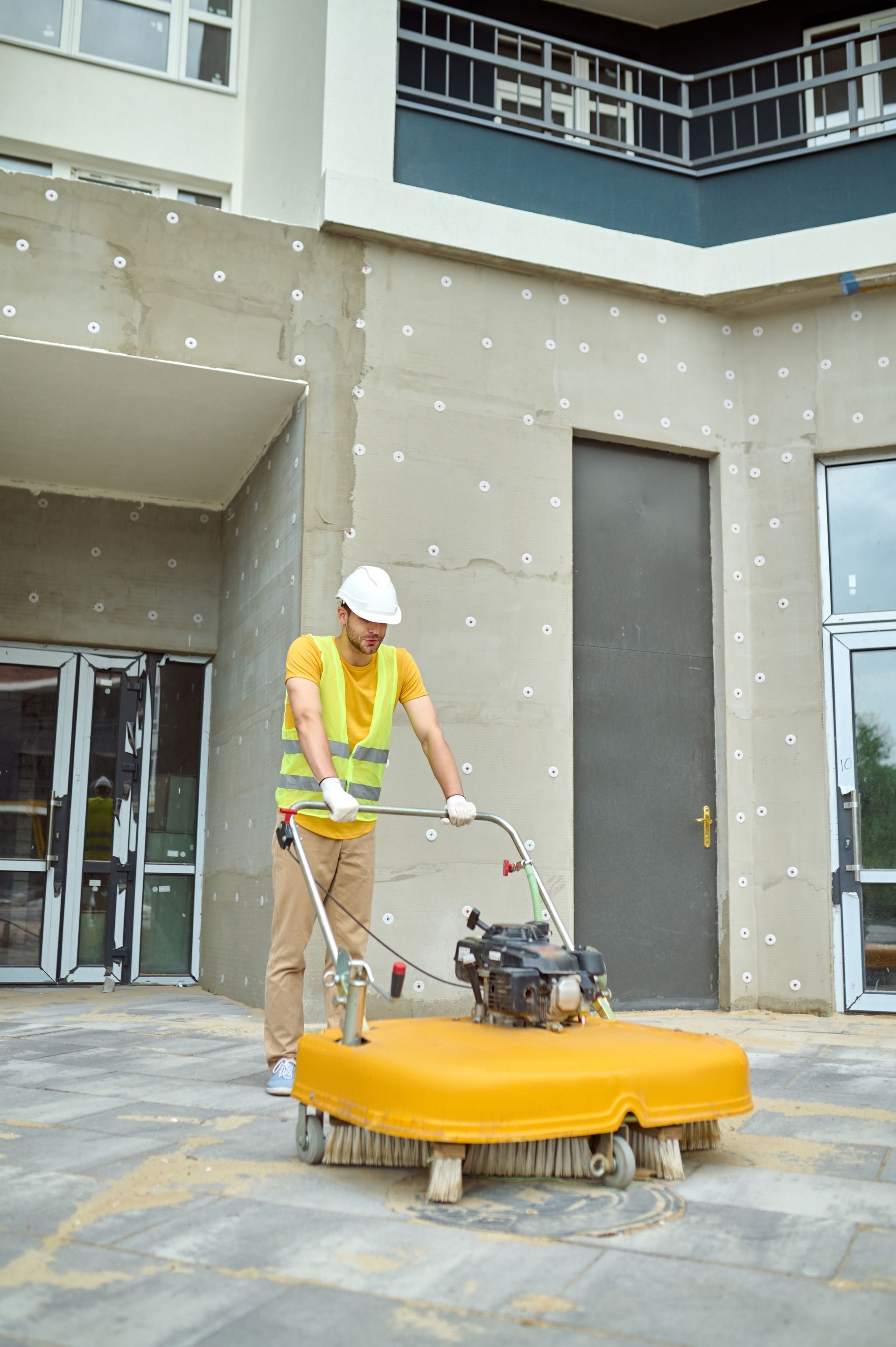 A man is using a machine to clean the sidewalk in front of a building.