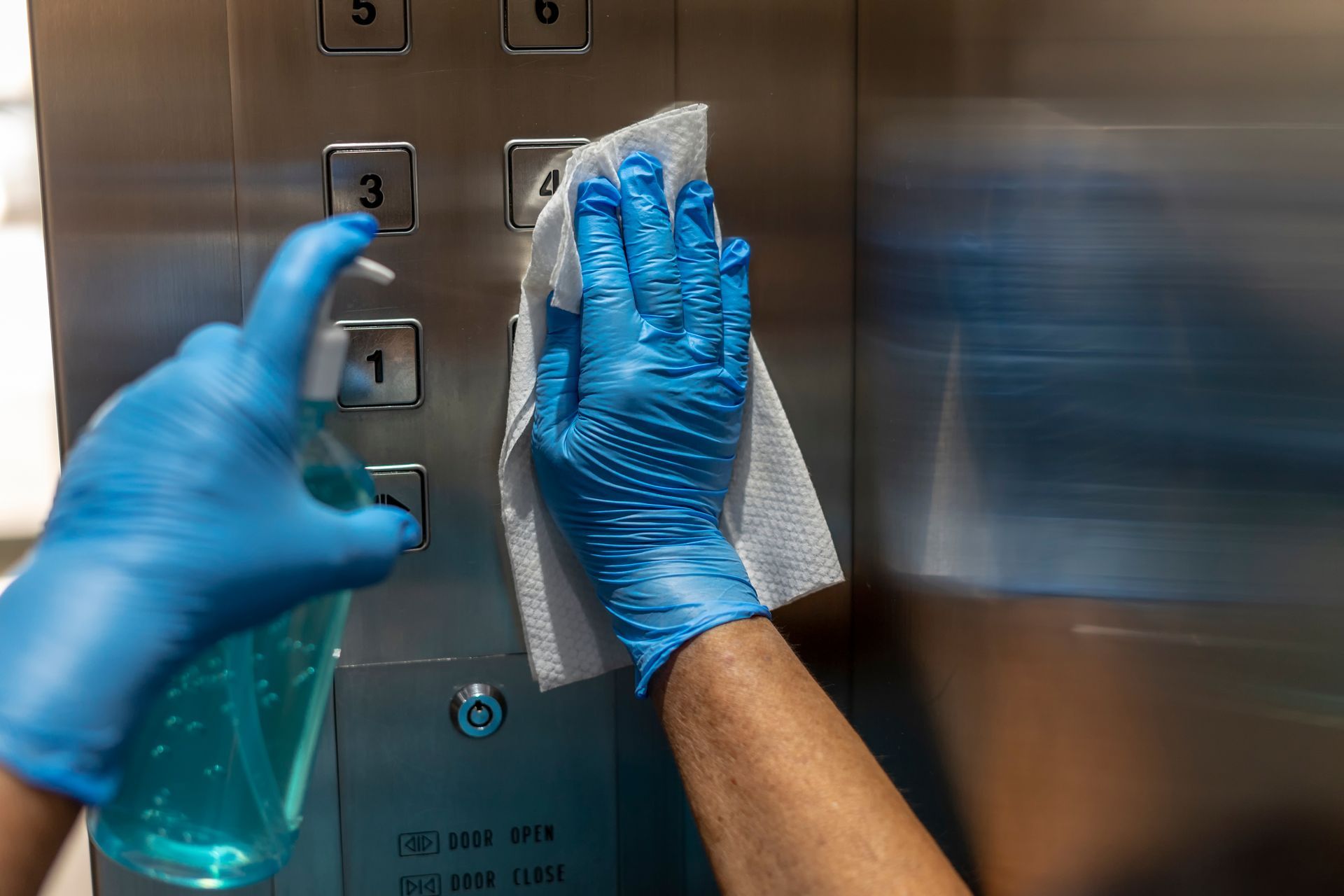 A person wearing blue gloves is cleaning an elevator with a cloth.