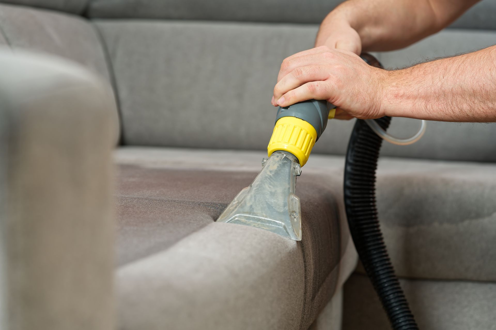 A man is cleaning a couch with a vacuum cleaner.