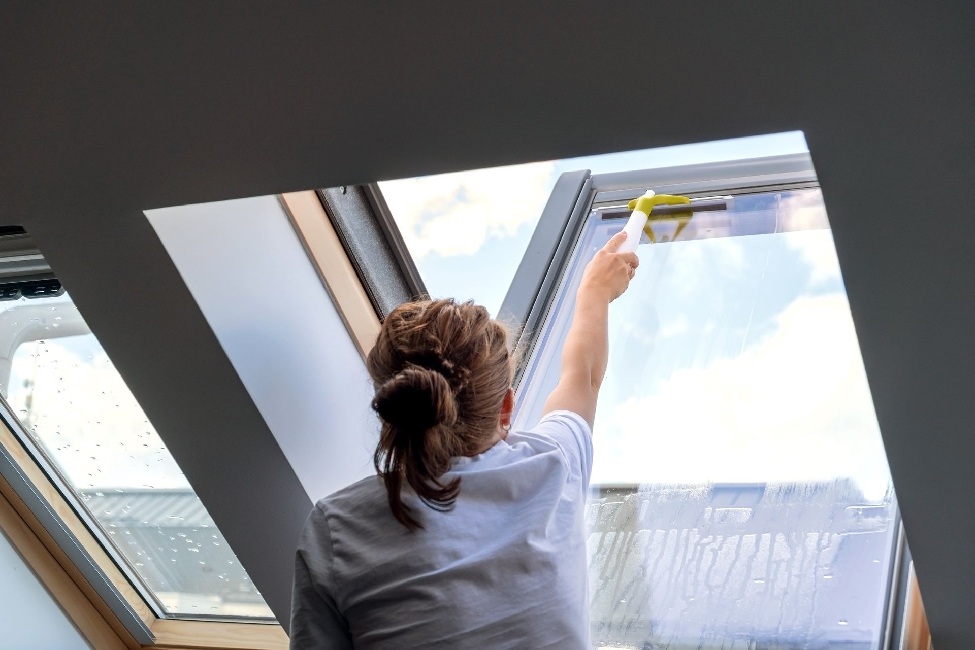 A woman is cleaning a skylight with a sponge.