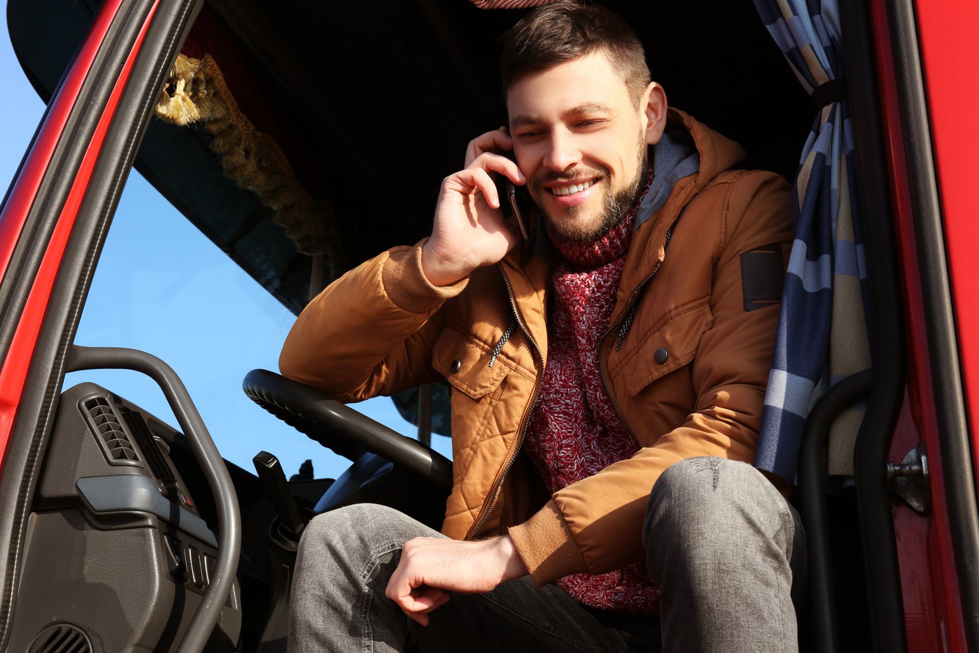Young truck driver sitting in truck on phone