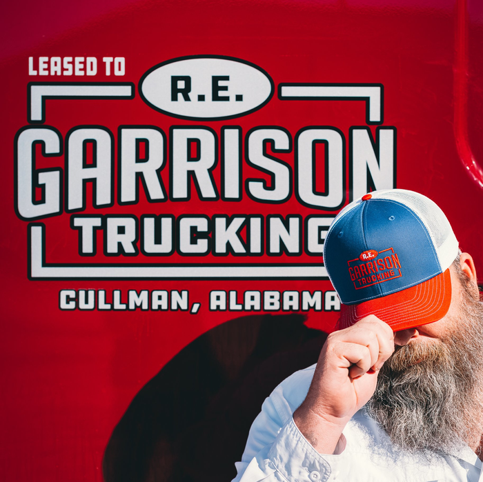 Trucker wearing R.E. Garrison Hat standing in front of Garrison Truck focused on Logo