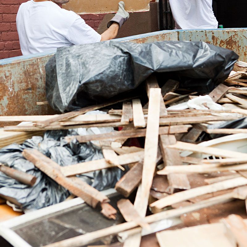 A man and a woman are loading wood into a dumpster.